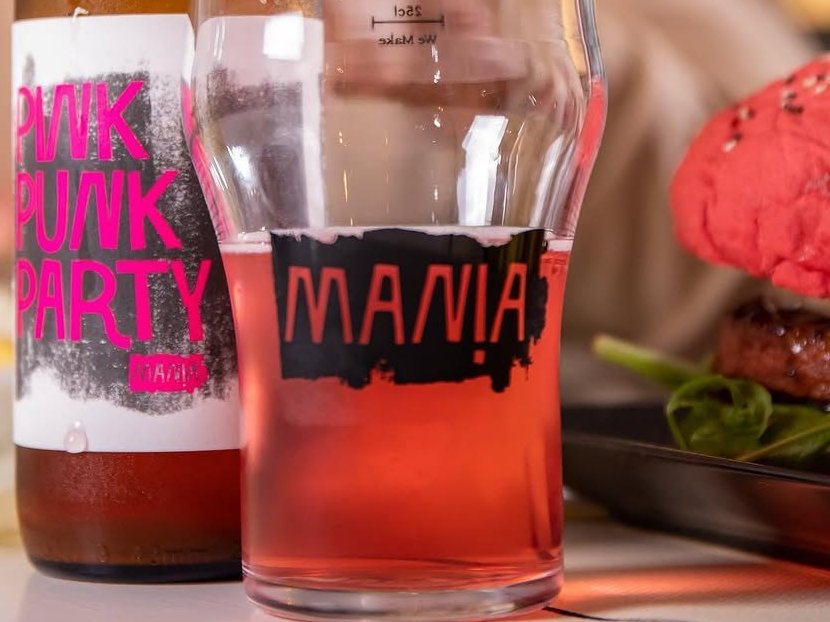 Garrafa e copo de cerveja artesanal rosada, com um hambúrguer em pão vermelho ao lado